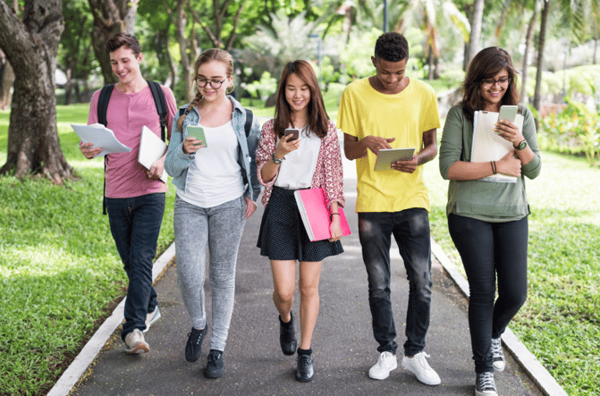 Five students walking in a horizontal line, all looking down at their phones and tablets