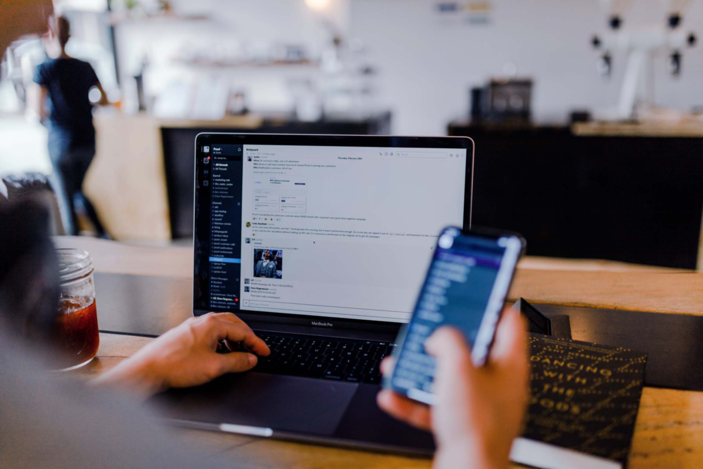 person holding phone and looking at laptop